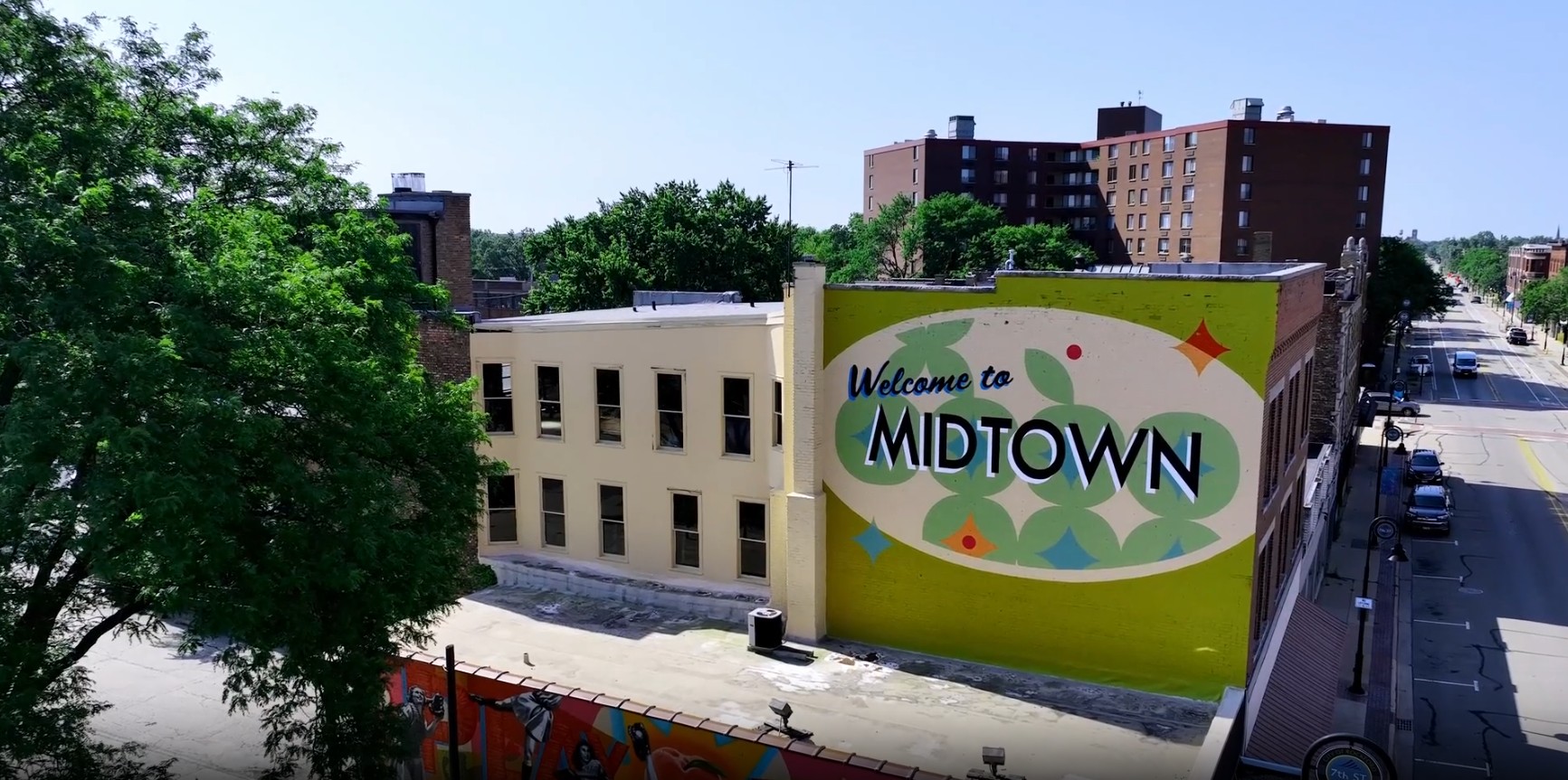 Image of the side of downtown buildings looking at a mural reading "Welcome to Midtown".
